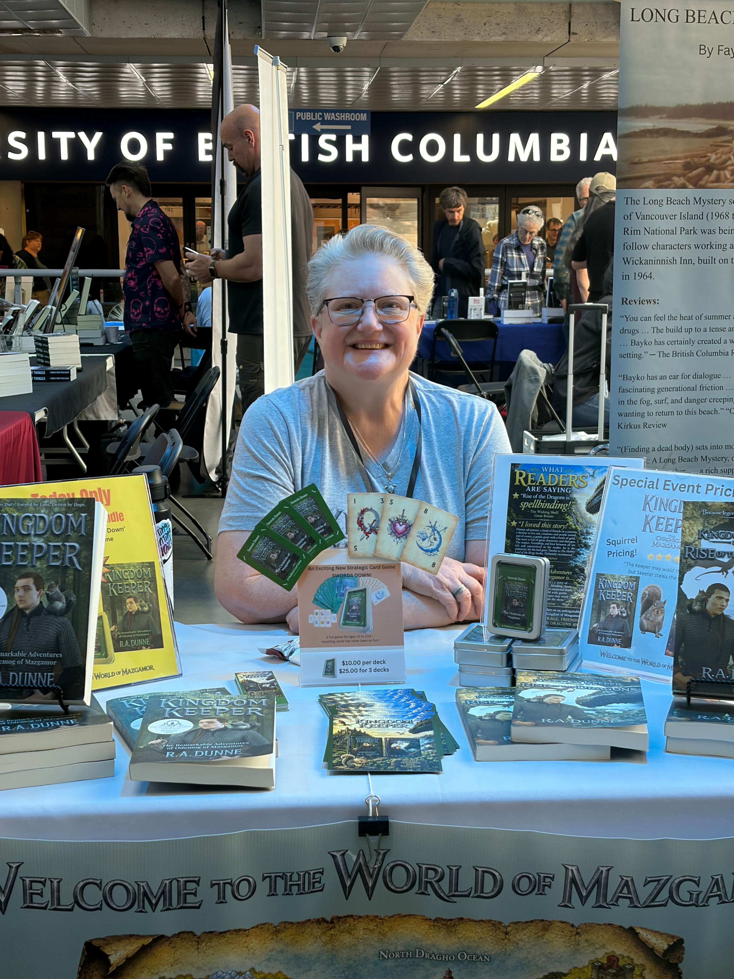 R.A. Dunne at a book fair event holding Swords Down card game with Kingdom Keeper display